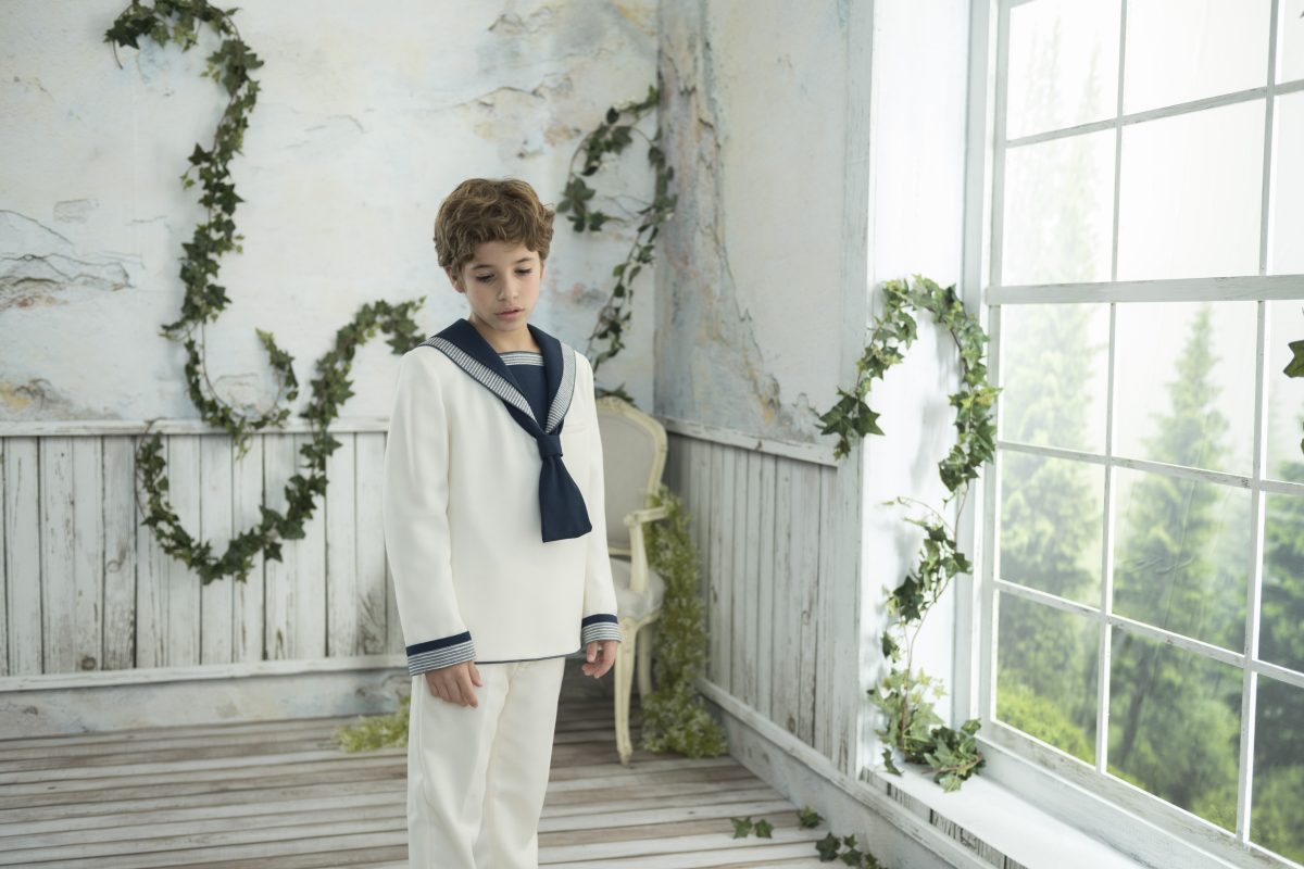 Traje de comunión marinero con blusa blanca, corbata azul marino y puños a contraste, combinado con un pantalón largo blanco.