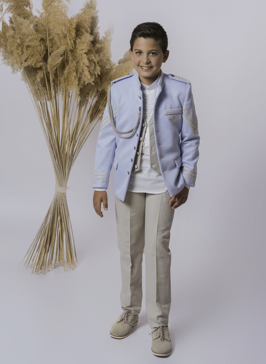Chaqueta azul celeste de comunión con bandas doradas y doble botonadura, combinada con un pantalón beige crema para crear contraste entre ambas prendas.