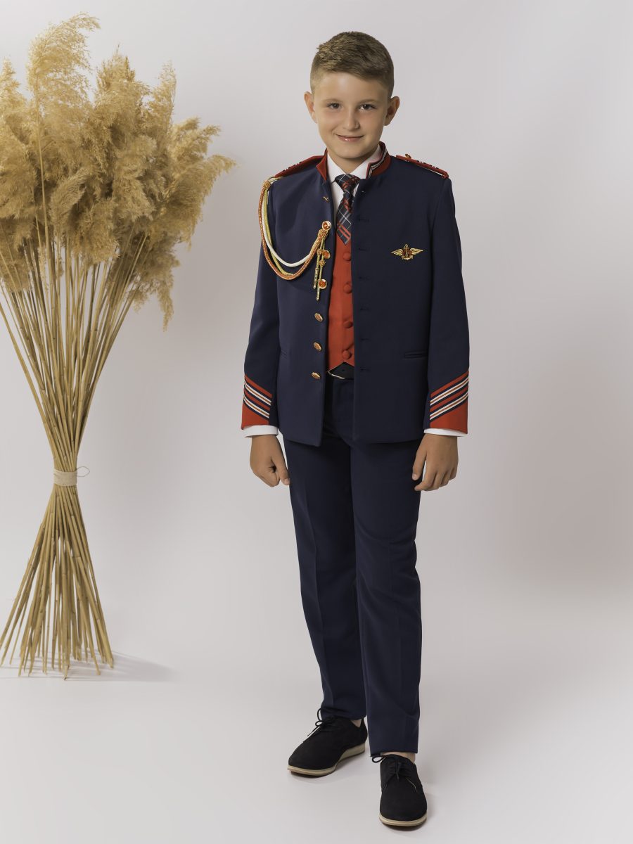 Traje de comunión azul marino de inspiración militar con ribetes rojizos, cordón dorado, chaleco rojo y corbata de cuadros sobre pantalón azul marino.