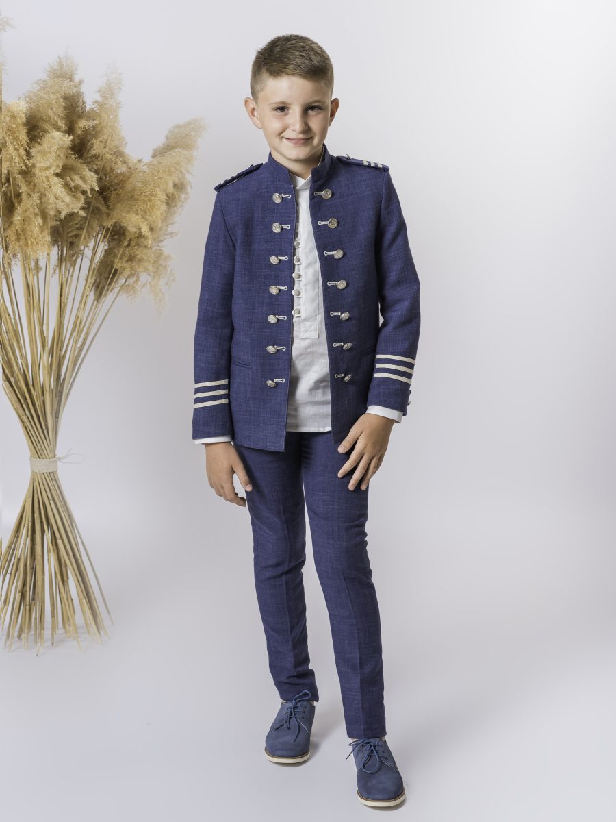 Traje de comunión azul marino con chaqueta de doble botonadura plateada, hombreras y franjas doradas en los puños, acompañado por camisa blanca.