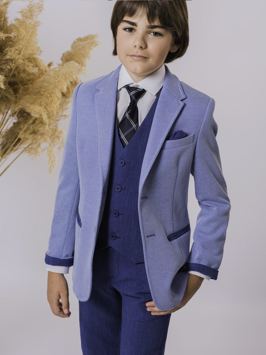 Detalle de un conjunto de comunión con chaqueta azul celeste, chaleco azul marino, corbata de cuadros y pañuelo oscuro en el bolsillo.