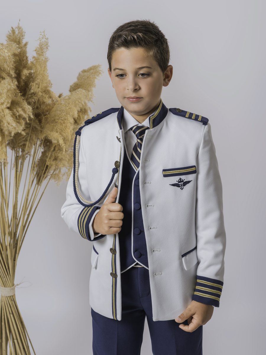 Detalle de chaqueta blanca de comunión con ribetes azul marino y dorados, cordón de hombro y chaleco oscuro junto a una corbata de rayas.