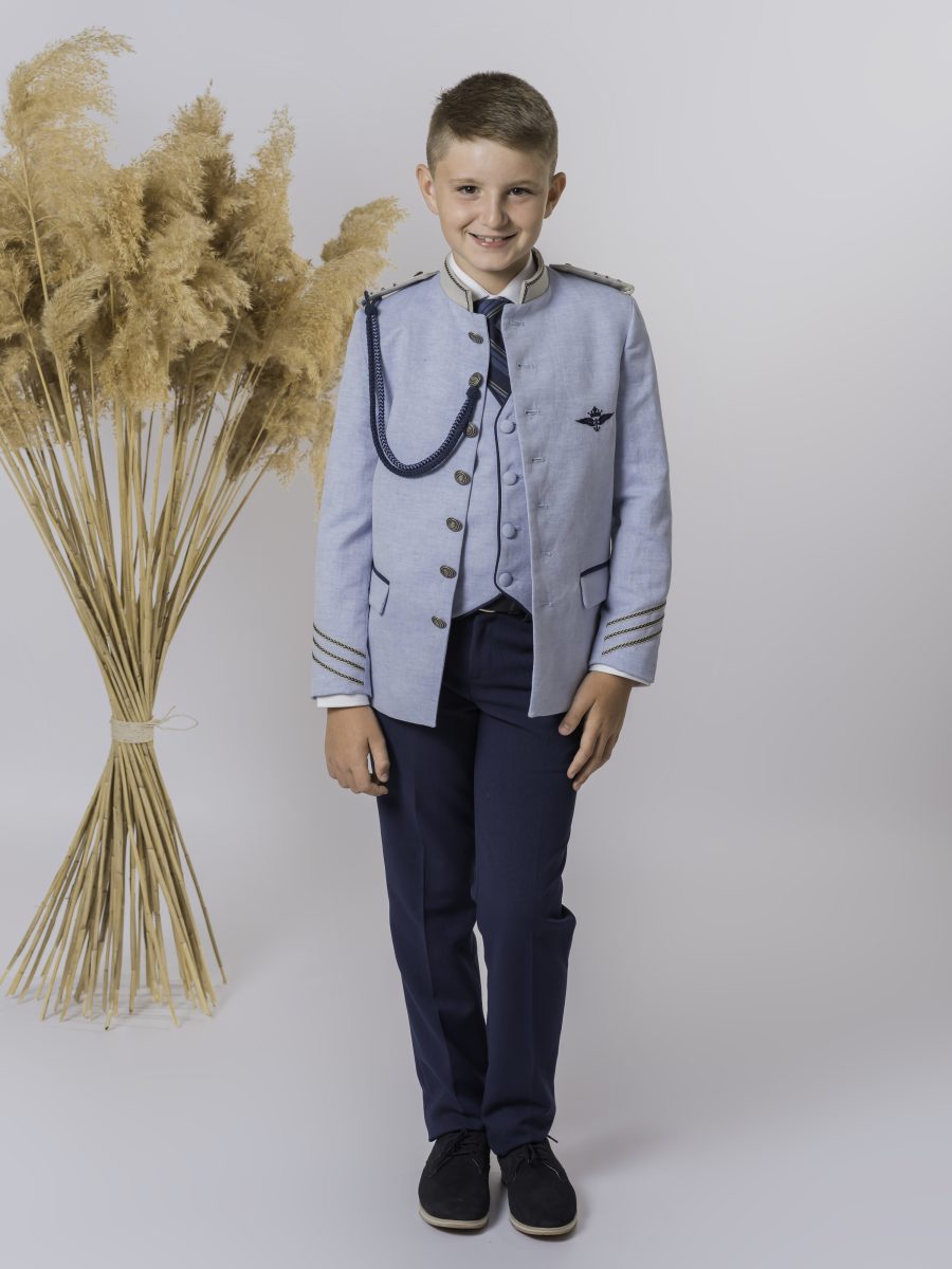 Traje de comunión con chaqueta azul celeste de ribetes oscuros, cordón de hombro y chaleco azul marino, combinado con corbata de rayas.
