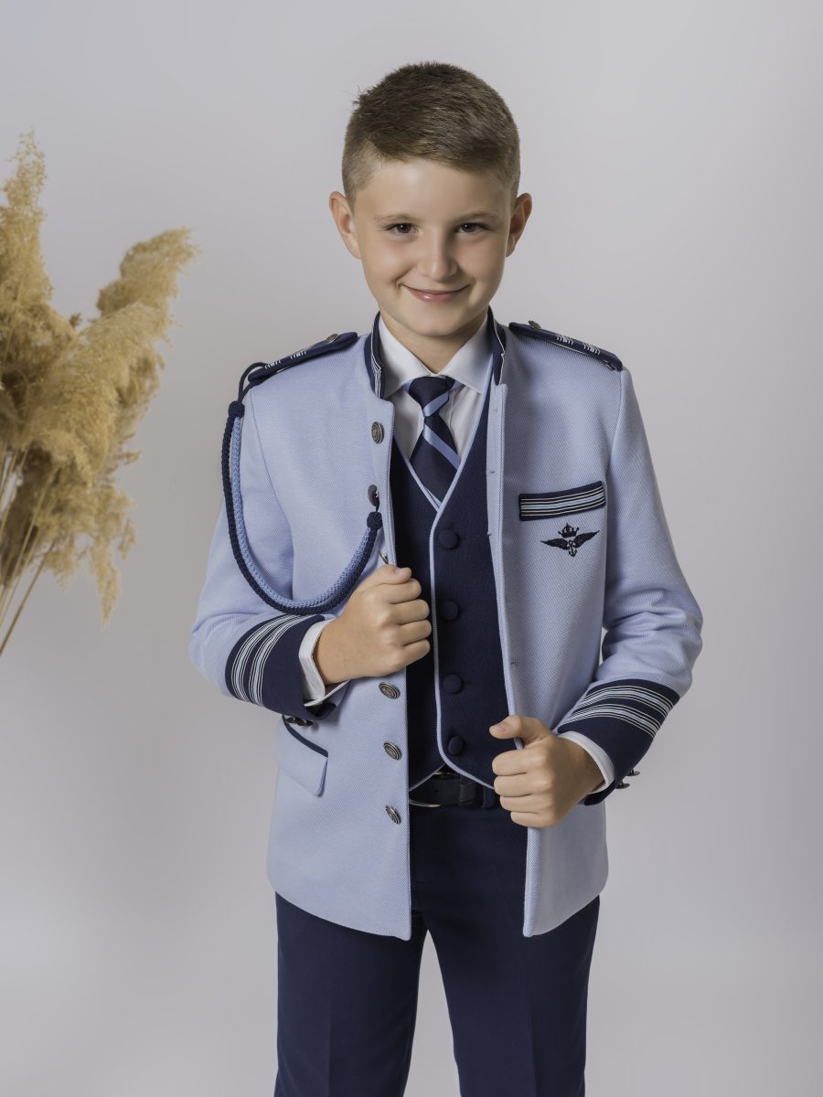 Detalle de chaqueta azul celeste de comunión con ribetes y cordón azul marino, insignia con corona y chaleco oscuro junto a una corbata de rayas.