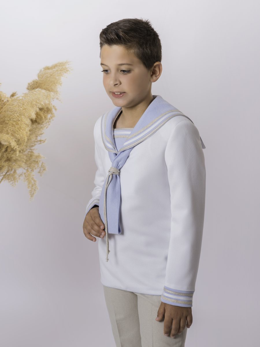 Detalle de blusa blanca marinera de comunión con cuello ribeteado en azul celeste y dorado, lazo azul y puños con galones dorados.