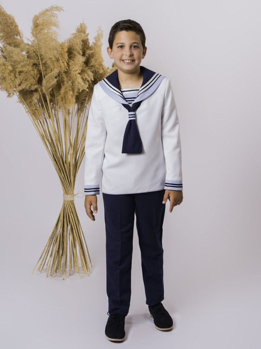 Traje marinero de comunión con blusa blanca de ribetes oscuros, corbata y puños azul marino, combinado con un pantalón del mismo azul.