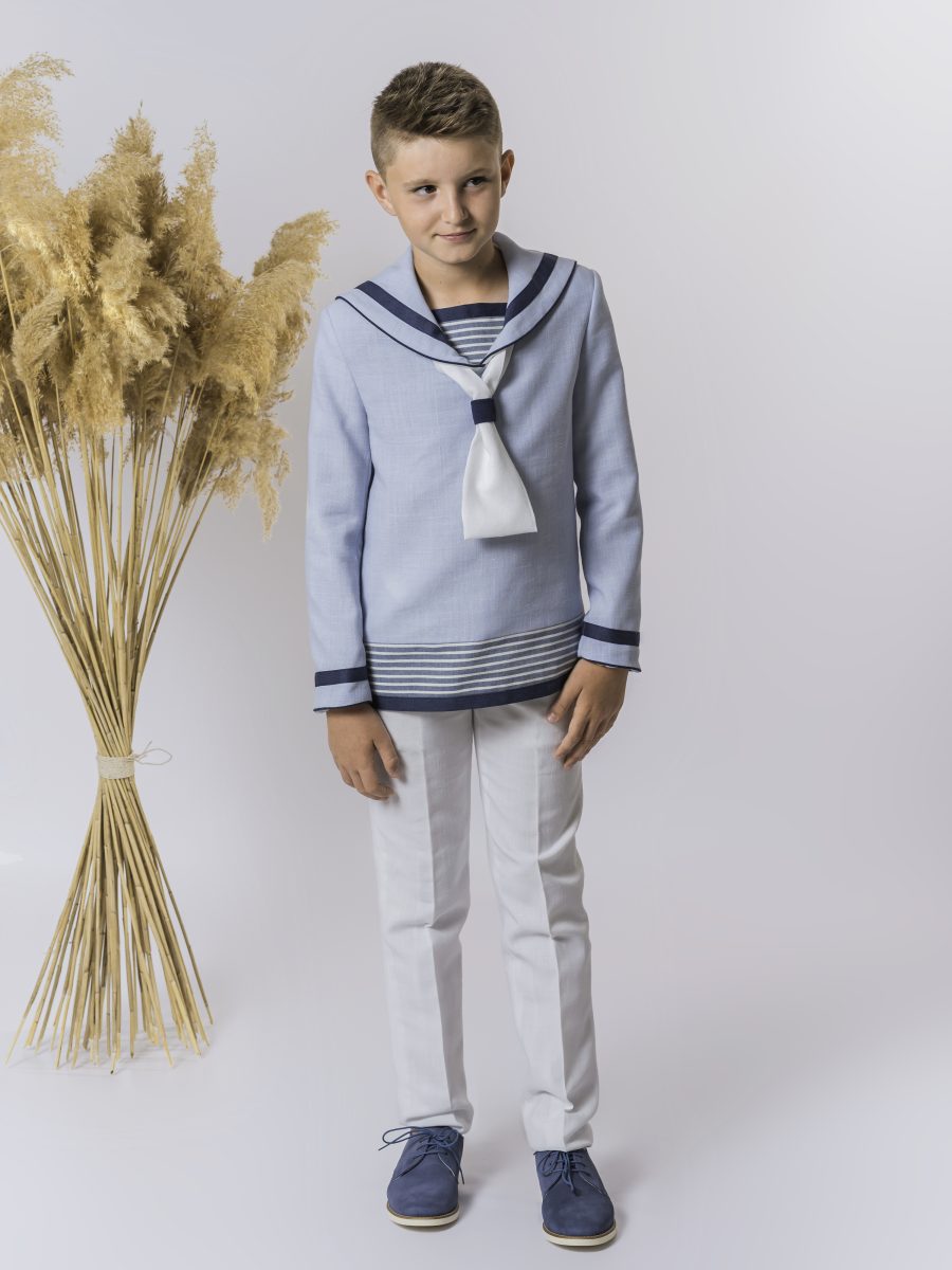 Traje marinero de comunión con blusa azul celeste, cuello de ribetes azul marino y lazo blanco, combinado con un pantalón blanco.