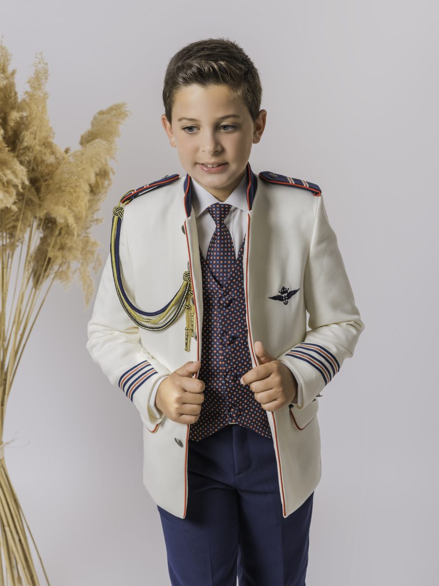 Chaqueta de comunión blanca marfil con ribetes rojos y azul marino, cordón dorado y oscuro, chaleco estampado y corbata de motivos rojos y azules.
