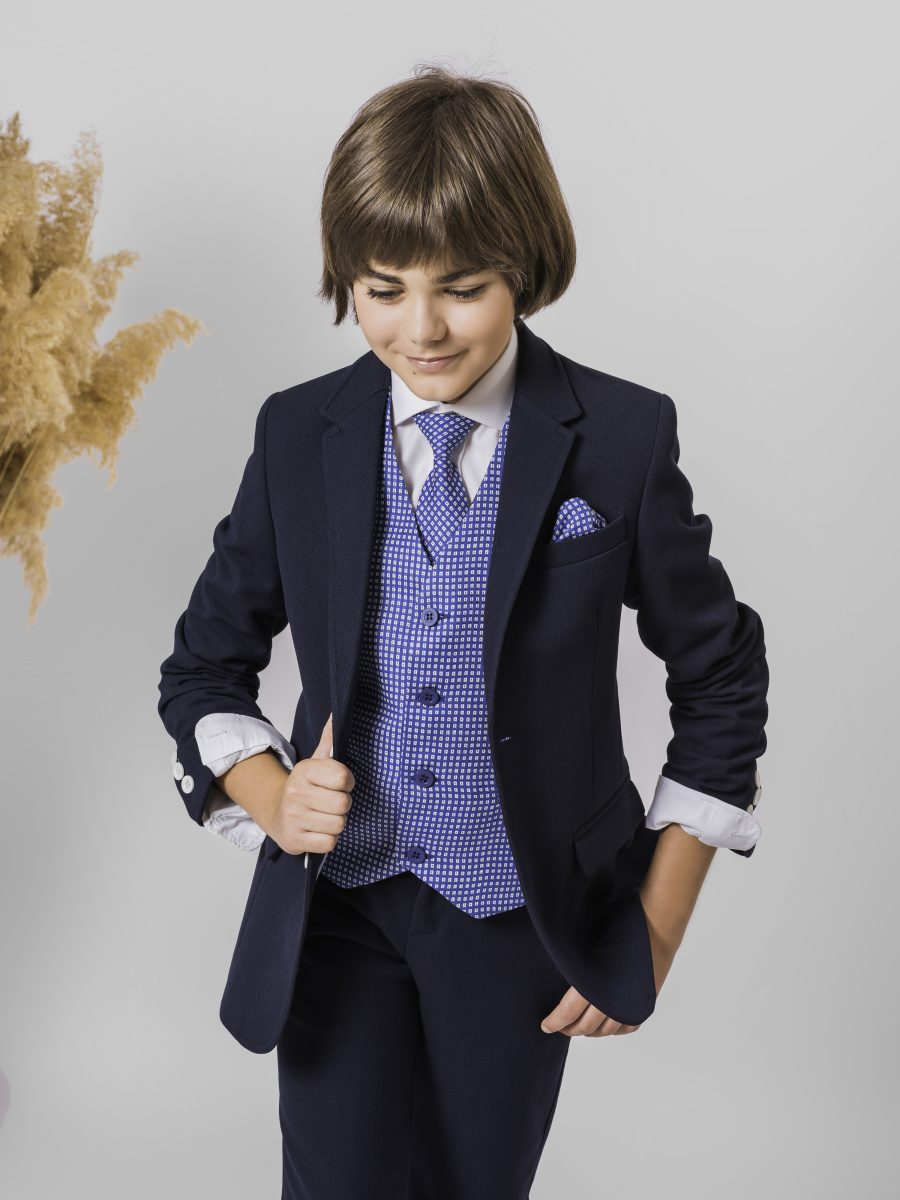 Detalle de traje de comunión azul marino con chaleco estampado azul y blanco, camisa blanca, corbata azul con dibujo y pañuelo en el bolsillo.