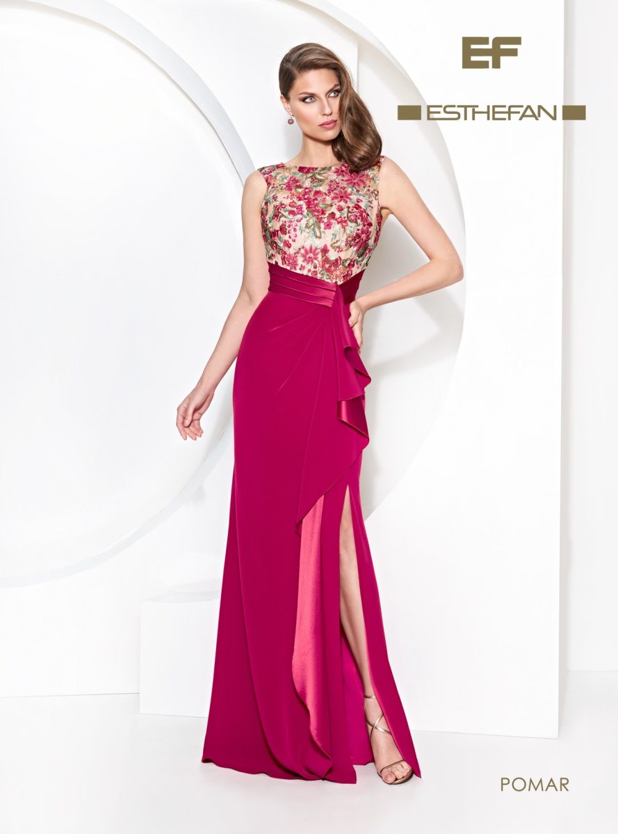 Vestido largo fucsia de Esthefan con cuerpo floral bordado, escote de transparencia, cinturón satinado y un volante diagonal sobre la falda.