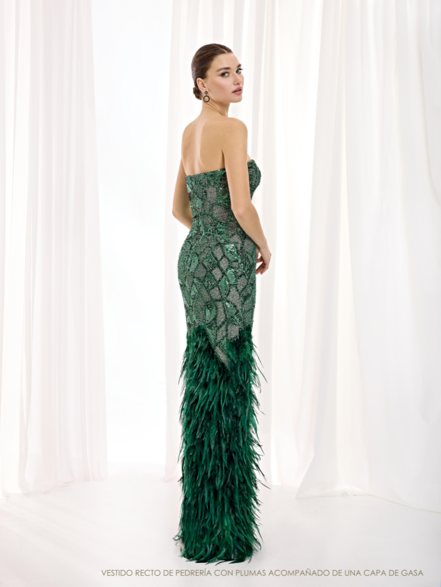 Espalda escotada del vestido de Esthefan sin la capa exterior, con cuerpo de decoración geométrica y plumas verdes en la parte inferior.