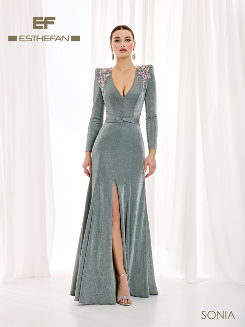 Vestido largo verde salvia metalizado de Esthefan con escote en V, mangas largas, flores de pedrería en los hombros y abertura frontal.
