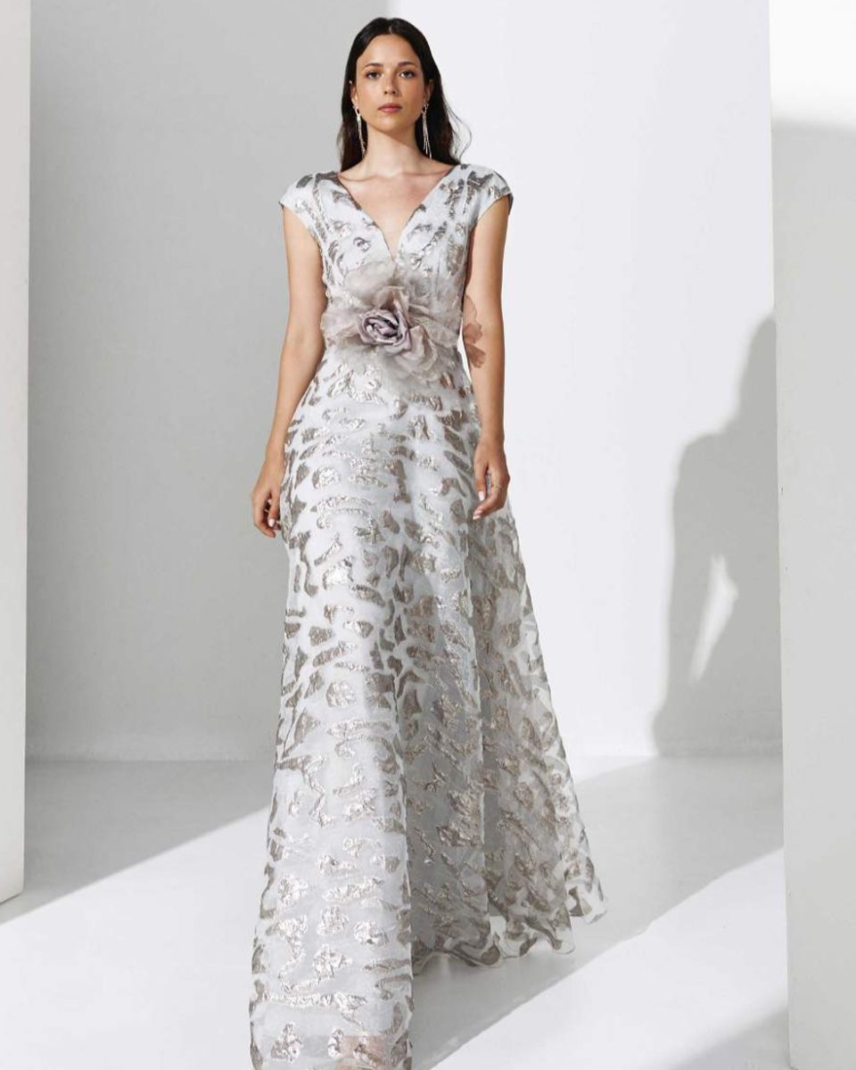 Vestido largo de María Coca con bordado floral en plata empolvado, escote en V, mangas cortas voluminosas y aplicación floral en la cintura.