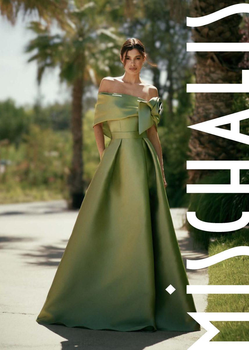 Vestido largo verde oliva de Mischalis con capelina drapeada, rosa central de gran volumen y falda amplia de pliegues profundos.
