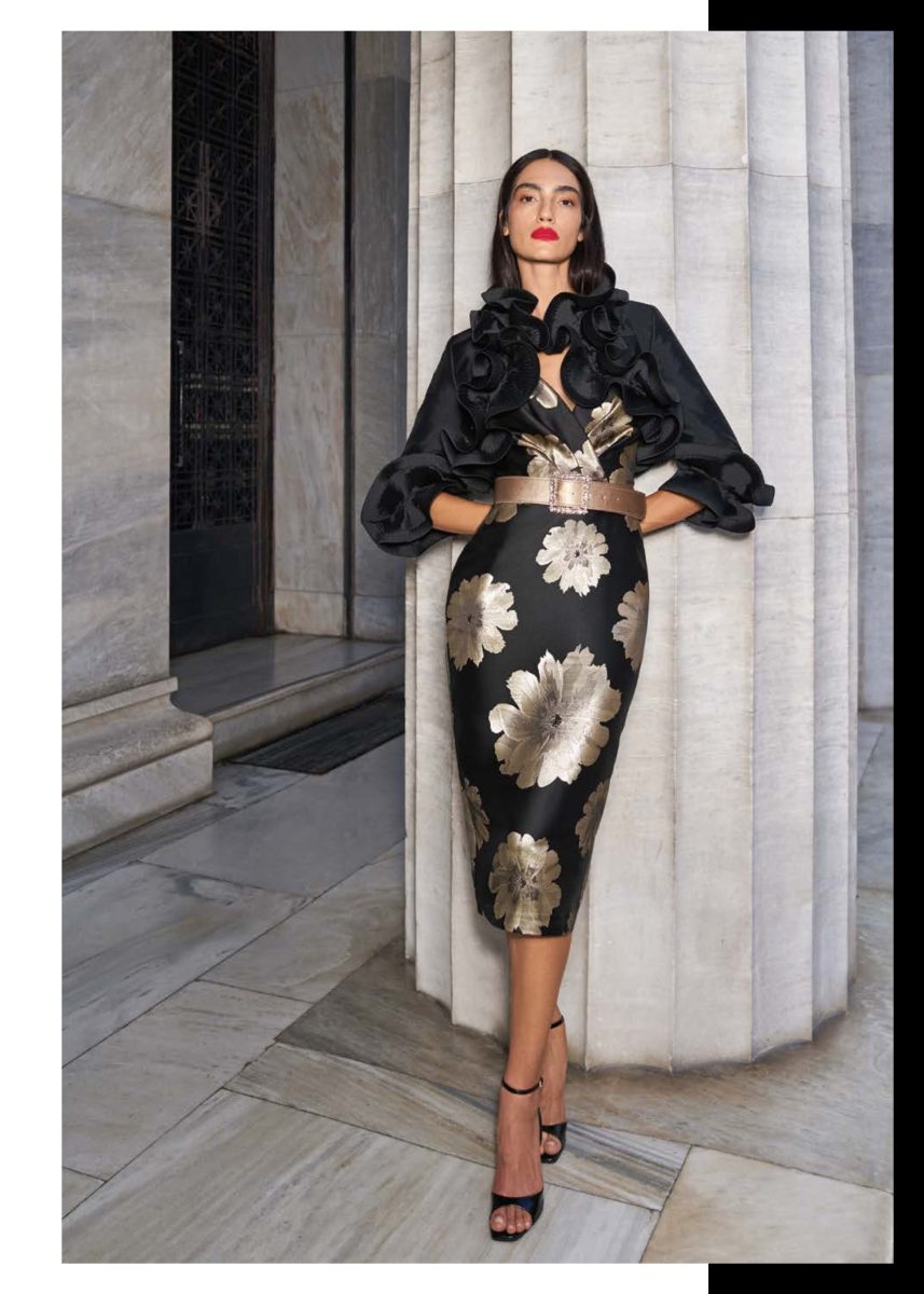 Vestido midi negro de Mischalis con flores doradas, acompañado de chaqueta de volantes florales negros y cinturón tostado con hebilla ornamentada.