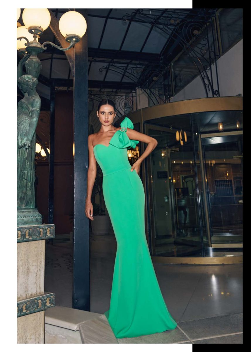 Vestido largo verde esmeralda de Mischalis con gran lazo y adorno joya en un hombro, cuerpo entallado y falda columna.