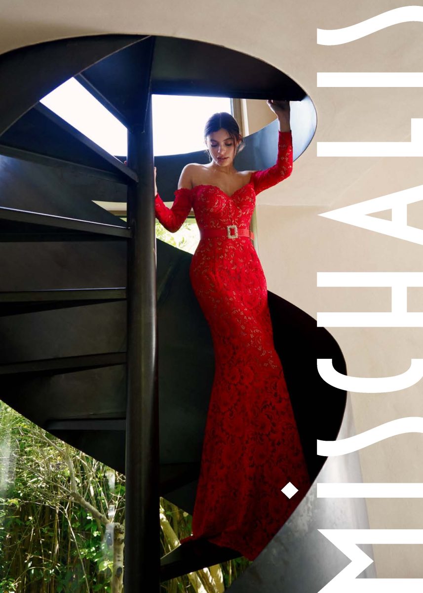 Vestido largo rojo de Mischalis con encaje floral sobre fondo nude, hombros descubiertos, mangas largas y cinturón con hebilla joya.