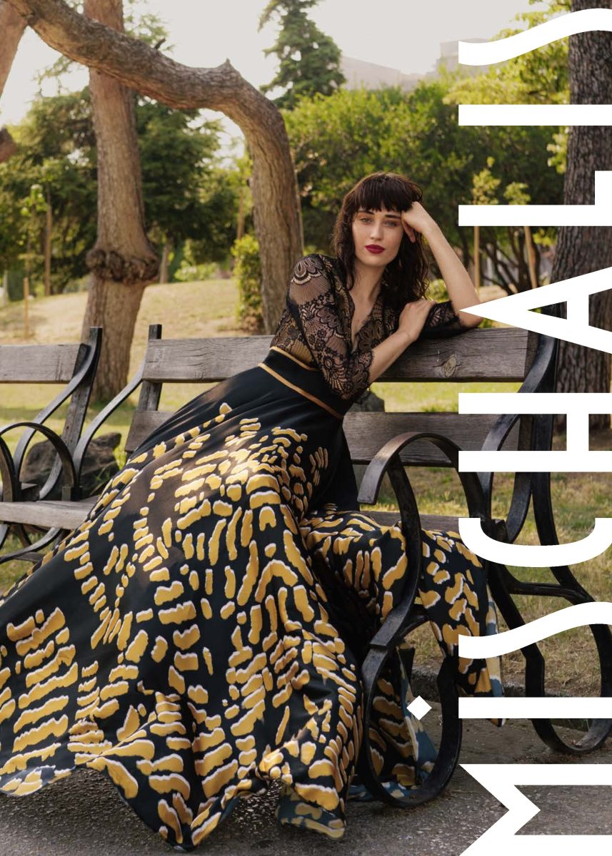 Vestido largo de Mischalis con cuerpo de encaje negro, mangas largas, cintura dorada y falda amplia con estampado abstracto dorado y negro.