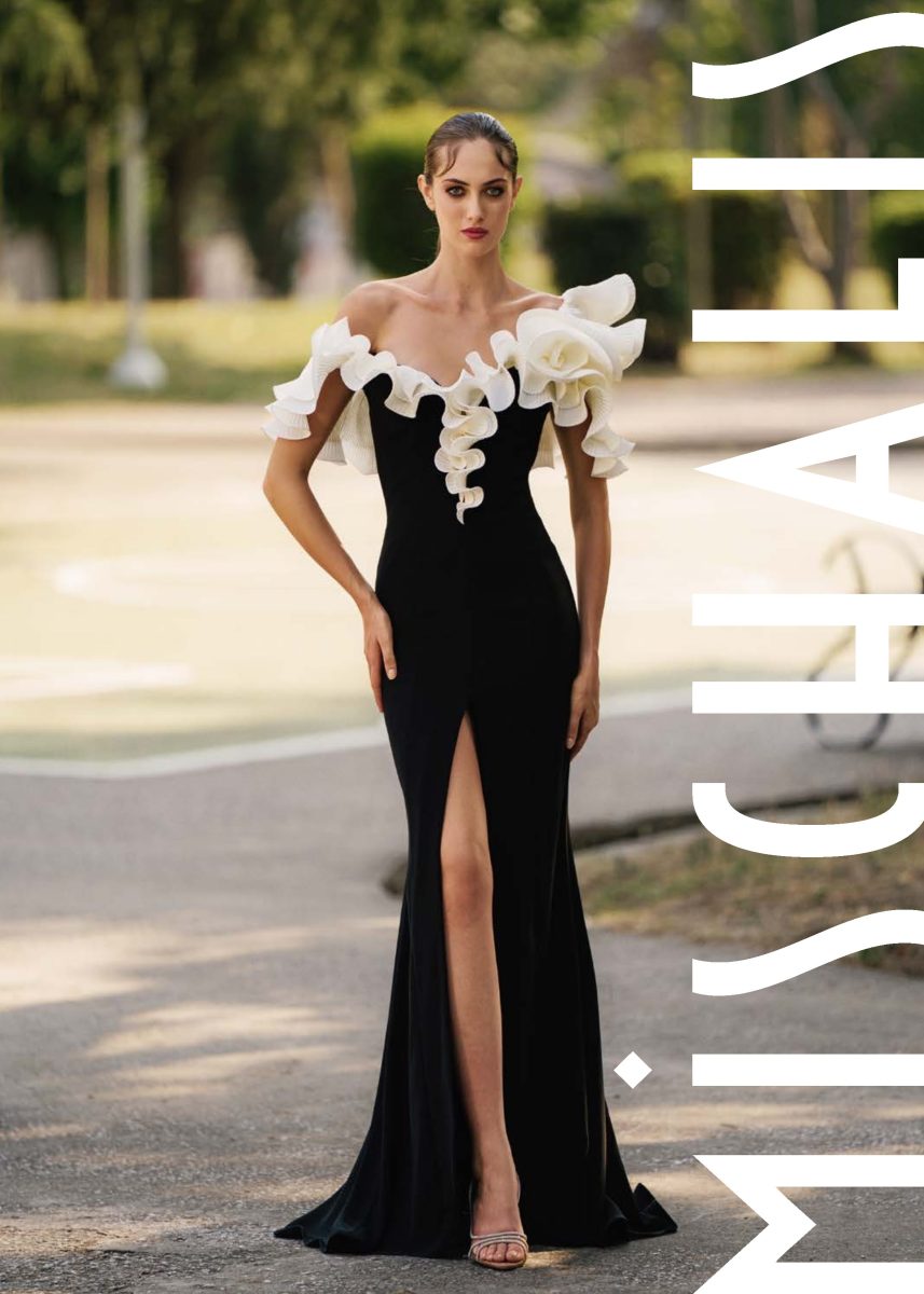 Vestido largo negro de Mischalis con volantes florales blancos y crema en el escote, cuerpo entallado, abertura lateral y ligera cola.