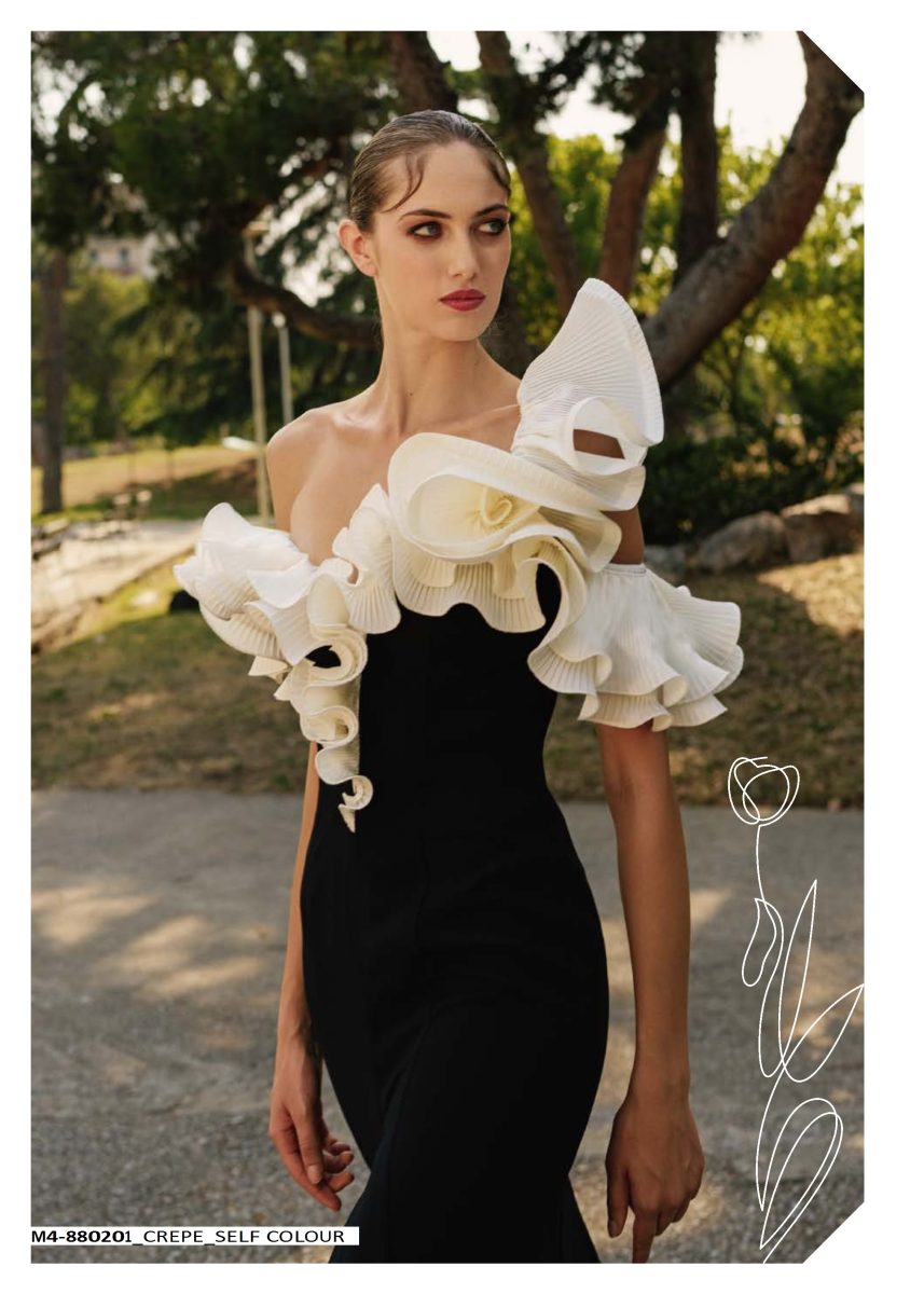 Detalle del escote del vestido negro de Mischalis, cubierto de volantes florales blancos y crema sobre el inicio del cuerpo entallado.