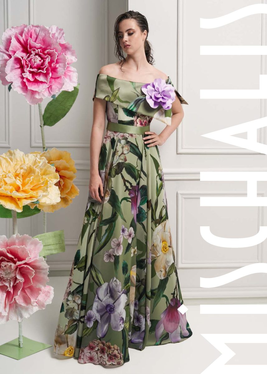 Vestido largo verde claro de Mischalis con flor lila en el hombro, capelina, cinturón verde y falda amplia de estampado botánico.